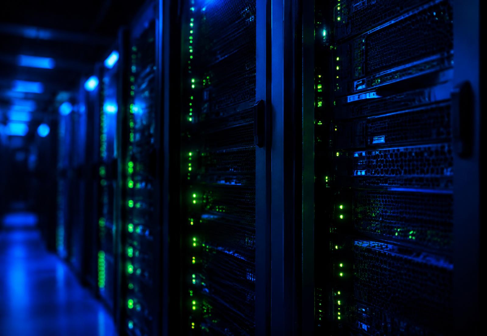Rows of server racks in a dark data center lit by blue light and green status LEDs